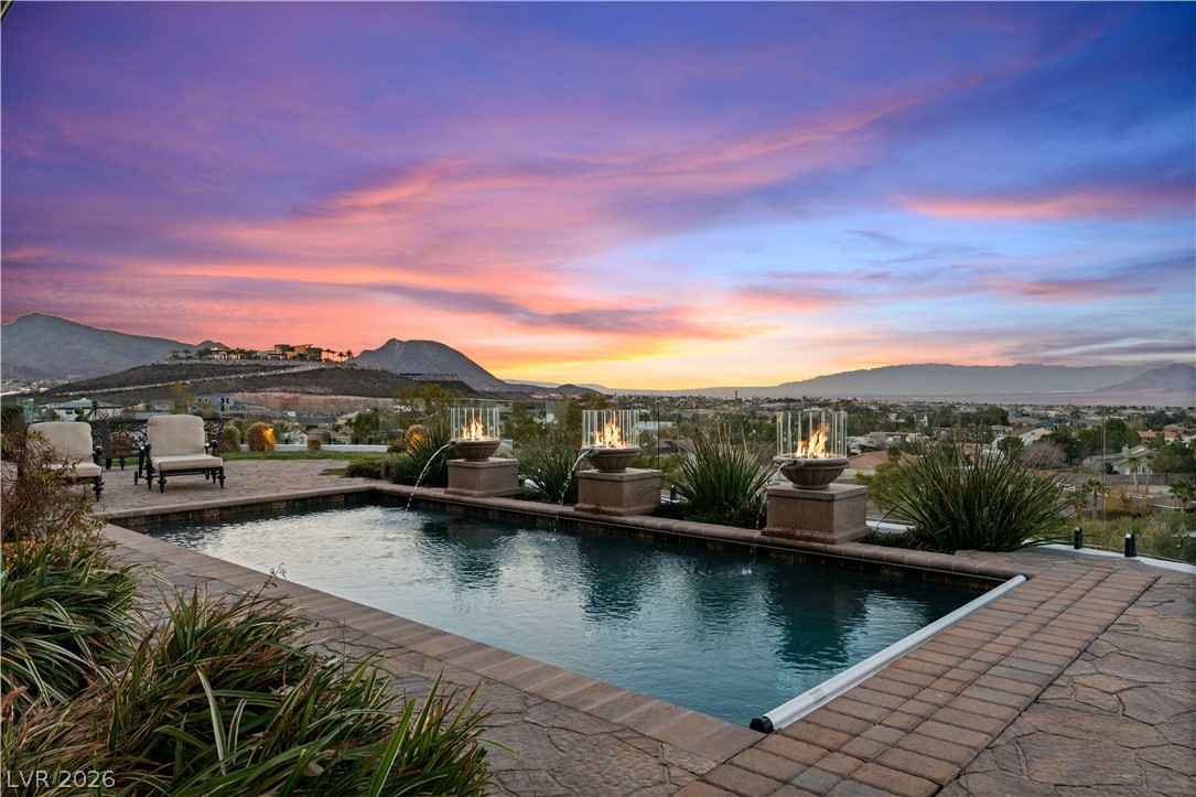 1123 Christian Road Henderson, NV 89002 - Photo 93 of 94 An inviting pool, complete with water features and fire accents, overlooks a breathtaking mountain landscape at sunset.