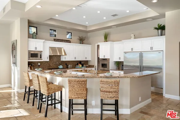 a kitchen with stainless steel appliances kitchen island granite countertop a table chairs and a refrigerator