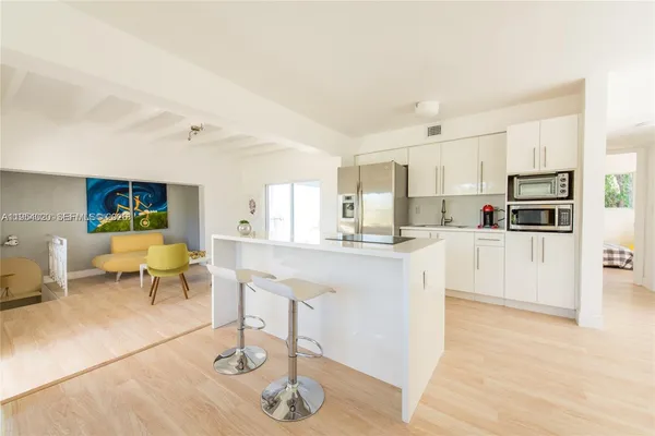 a kitchen with stainless steel appliances kitchen island granite countertop a refrigerator a stove a sink and white cabinets with wooden floor