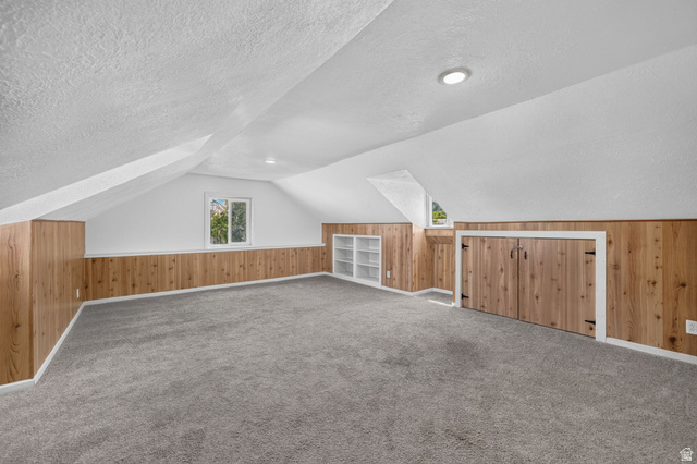220 East Greenwood Avenue Midvale, UT 84047 - Photo 26 of 46 Spacious room featuring sloped ceilings, two windows, wood-panel accent walls, and soft grey carpeting