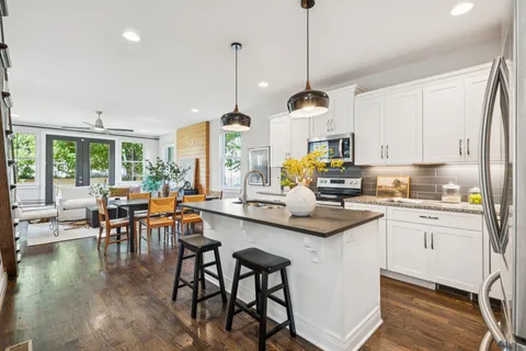 a kitchen with stainless steel appliances granite countertop a stove top oven a sink a dining table and chairs with wooden floor