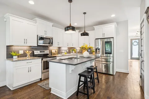 a kitchen with stainless steel appliances kitchen island granite countertop a refrigerator a stove a sink and white cabinets with wooden floor