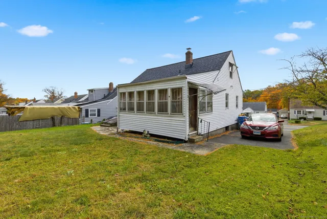 a white house that has a small yard and couches chairs with wooden fence