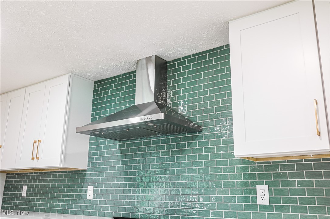 55 Elm Street Rittman, OH 44270 - Photo 16 of 46 Kitchen view of wall chimney exhaust hood, white cabinetry, backsplash, and a textured ceiling