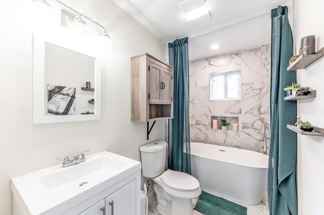 a bathroom with a bathtub shower sink vanity mirror and toilet