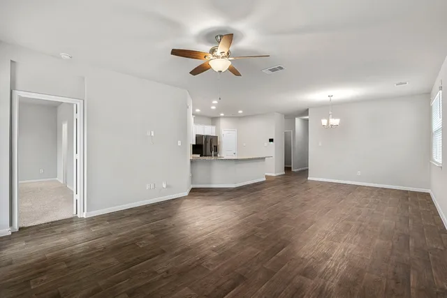 a view of an empty room with wooden floor and a ceiling fan
