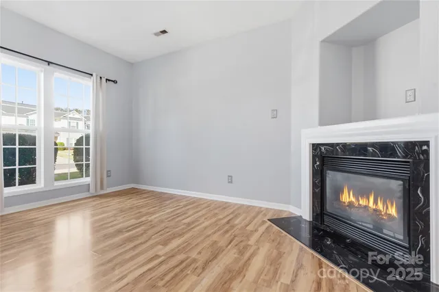 a view of an empty room with wooden floor fireplace and a window
