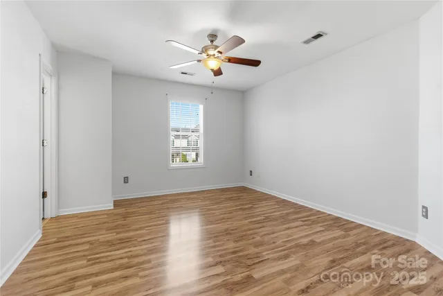an empty room with wooden floor chandelier fan and windows