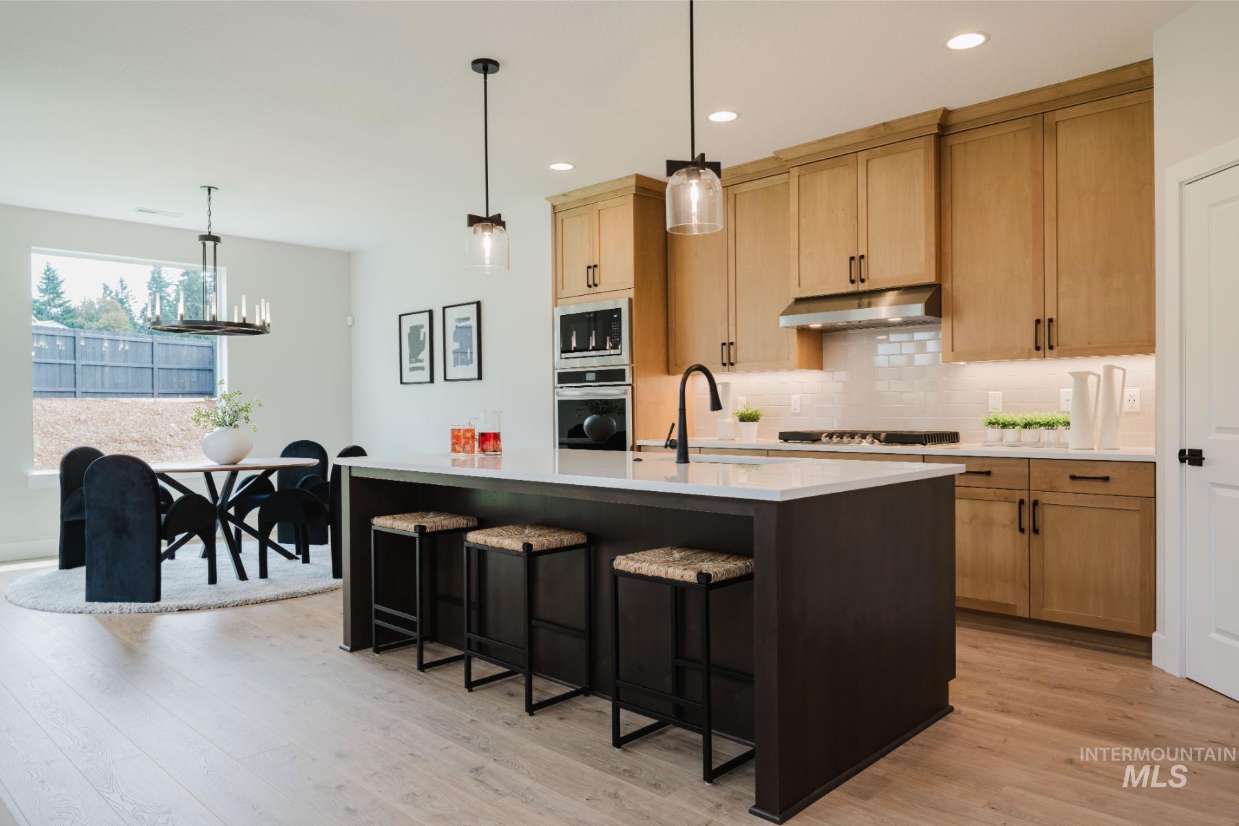 2866 North Stone Mill Avenue, Unit ROUGE Eagle, ID 83616 - Photo 4 of 18 Kitchen with pendant lighting, backsplash, a kitchen bar, a kitchen island with sink, and light wood-style floors