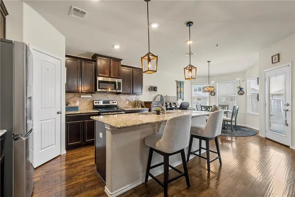 a kitchen with stainless steel appliances granite countertop a sink a stove a refrigerator cabinets a dining table and chairs