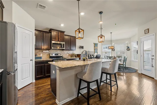 a kitchen with stainless steel appliances granite countertop a sink a stove a refrigerator cabinets a dining table and chairs