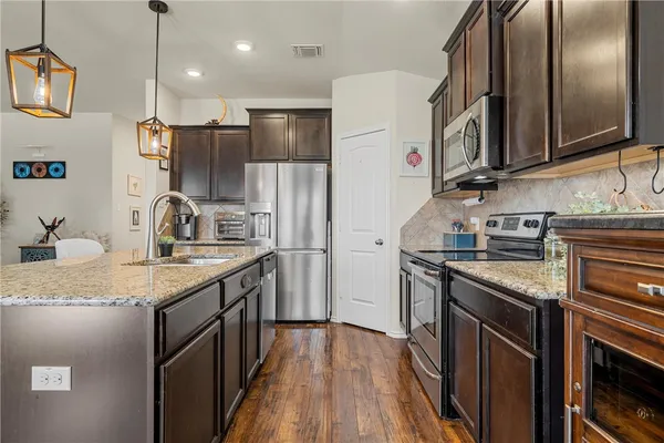 a kitchen with granite countertop stainless steel appliances a sink stove top oven and refrigerator