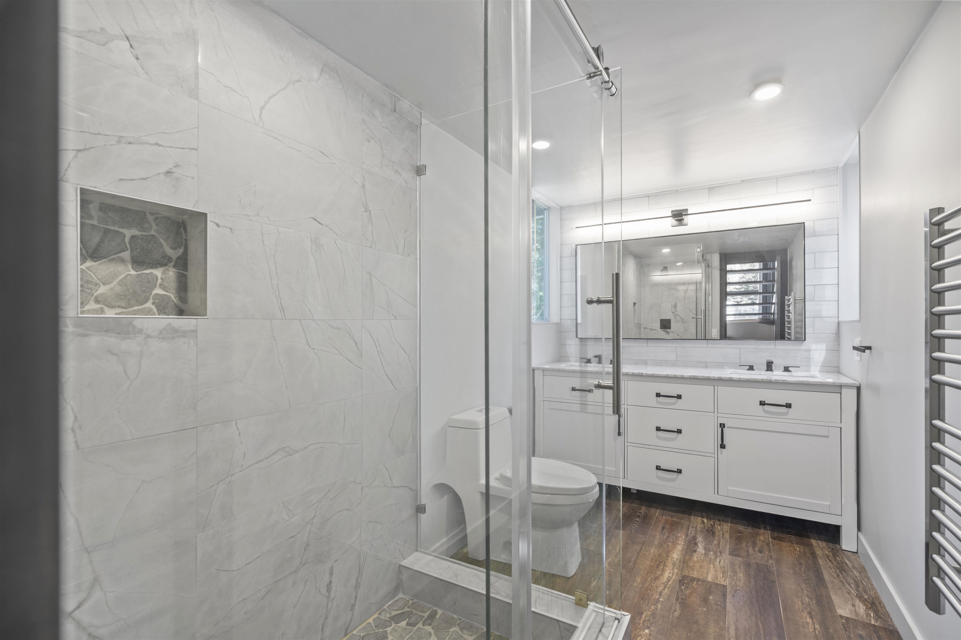 2570 Old Mammoth Road Mammoth Lakes, CA 93546 - Photo 23 of 39 Contemporary bathroom featuring a glass-enclosed shower with stone-tiled niche and floor, a dual vanity with undermount sinks and dark fixtures, and wood-finish flooring