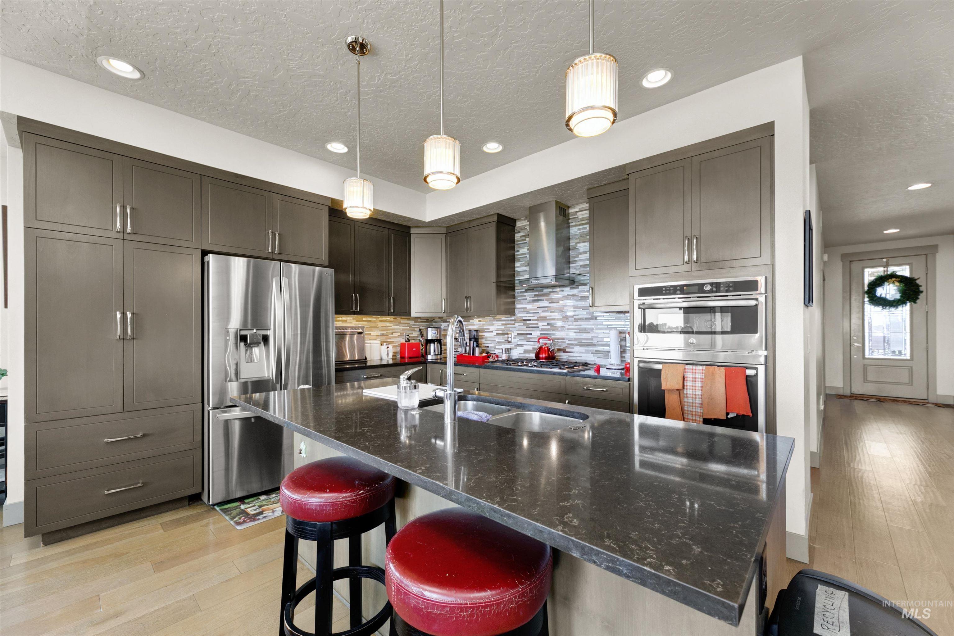 24398 Tombstone Ridge Court Middleton, ID 83644 - Photo 18 of 47 Modern kitchen featuring dark grey cabinetry, stainless steel appliances, a stone countertop island with an undermount sink, and light wood-finish flooring