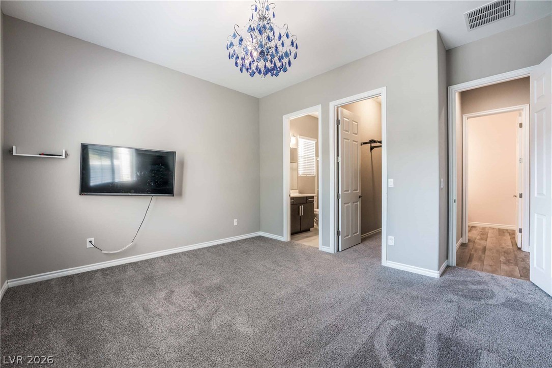 2787 Athens Ridge Drive Henderson, NV 89052 - Photo 10 of 31 A striking blue chandelier illuminates this spacious bedroom, offering comfort and convenience with ensuite access.