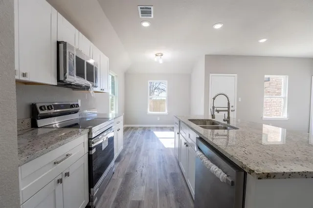 a kitchen with stainless steel appliances granite countertop a stove a sink dishwasher and microwave with wooden floor