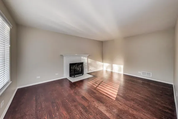 a view of an empty room with wooden floor fireplace and a window