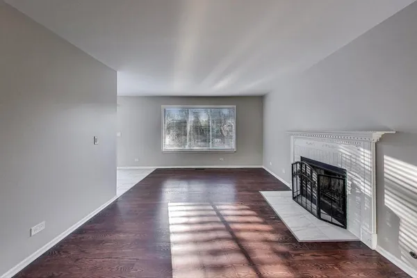 a view of an empty room with wooden floor fireplace and a window