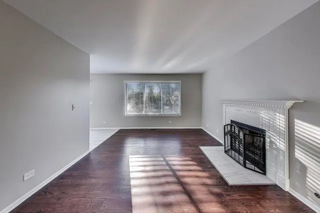 a view of an empty room with wooden floor fireplace and a window