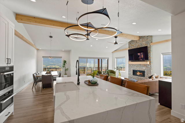 4499 North Seven Bridges Road, Unit 9 Eden, UT 84310 - Photo 6 of 65 Vaulted ceiling with exposed wood beams, stone fireplace, large sliding glass doors, white shaker cabinetry, and a large kitchen island with integrated sink
