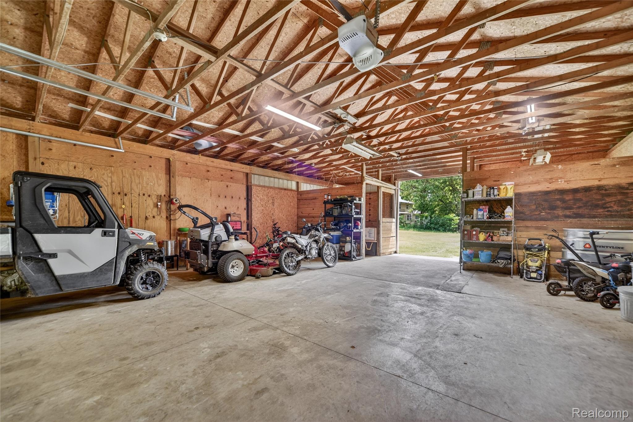 13635 Unadilla Road Gregory, MI 48137 - Photo 52 of 68 Spacious barn interior featuring an exposed wood truss ceiling, concrete flooring, plywood walls, fluorescent lighting, and an open entryway to the exterior