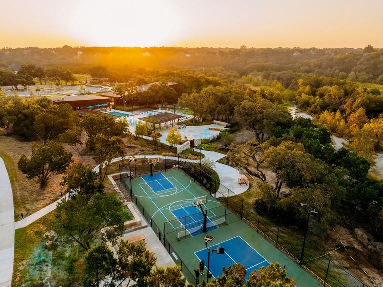 208 Wolf Springs Road Georgetown, TX 78628 - Photo 28 of 32 An aerial perspective reveals a vibrant community hub with multiple courts and shimmering pools amidst lush, mature trees.
