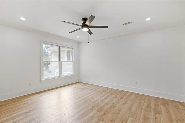 an empty room with wooden floor fan and windows