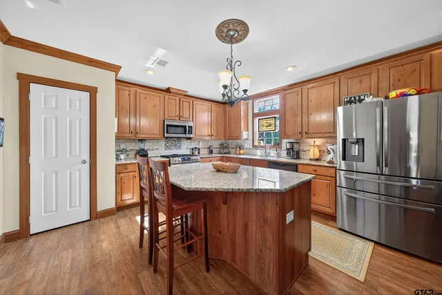 a kitchen with stainless steel appliances granite countertop a refrigerator a sink dishwasher a stove a refrigerator and island with wooden floor