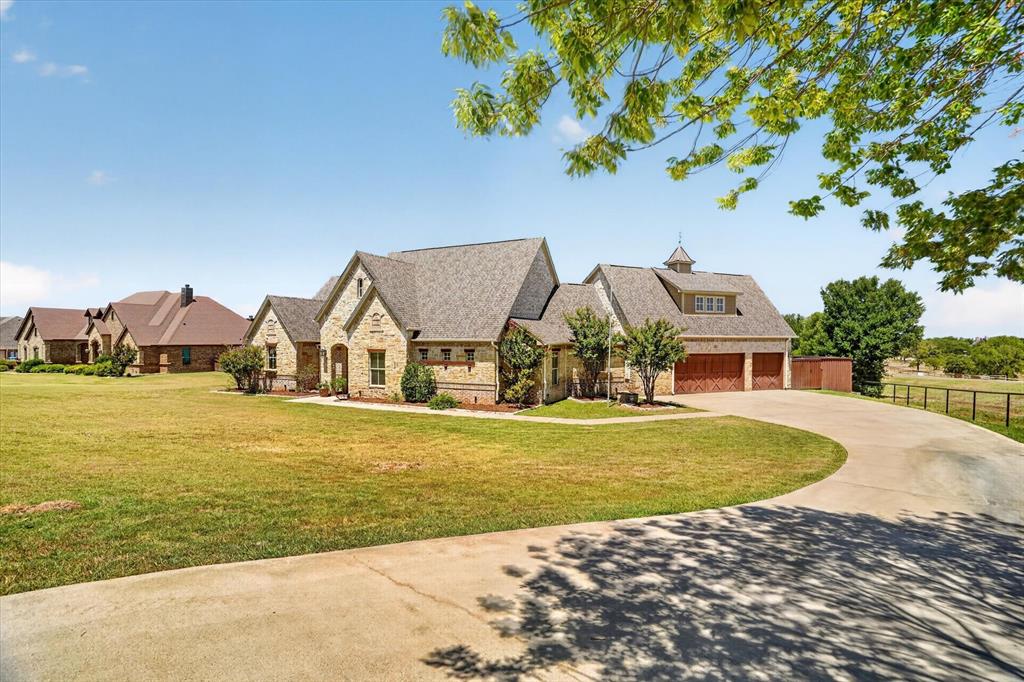 Elegant stone and stucco residence set on expansive manicured grounds featuring a circular driveway, mature landscaping, and a three-car garage