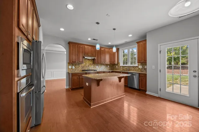 a kitchen with kitchen island granite countertop wooden floors stainless steel appliances a sink and a window