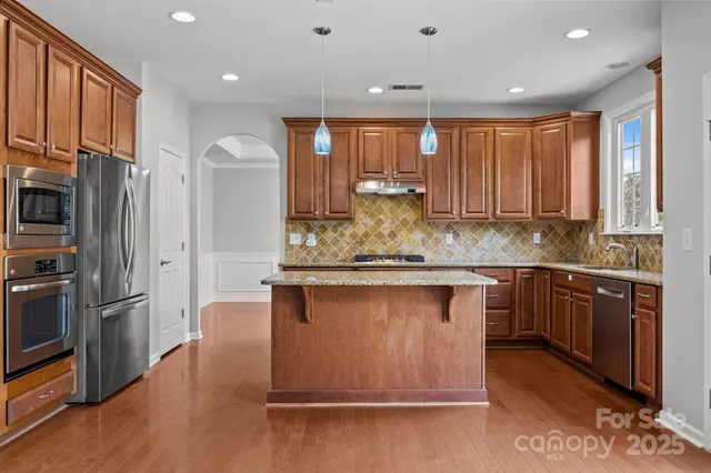 a kitchen with stainless steel appliances granite countertop wooden cabinets a refrigerator and dishwasher a oven with wooden floors