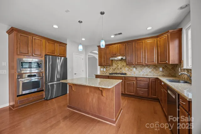 a kitchen with stainless steel appliances granite countertop a refrigerator a sink dishwasher a stove and white countertops with wooden floor
