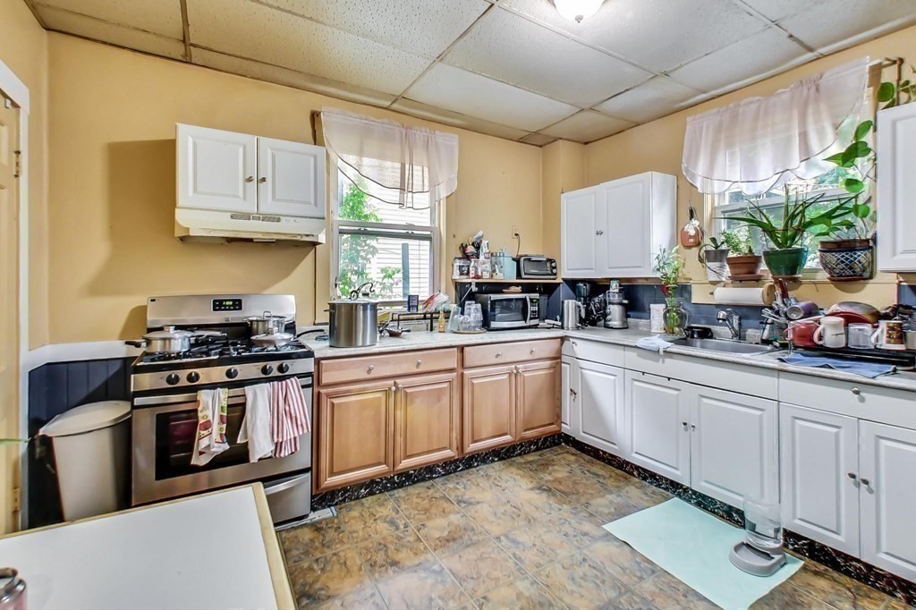 109 Walnut Street Somerville, MA 02145 - Photo 15 of 42 a white kitchen with stainless steel appliances granite countertop a stove a sink dishwasher and white cabinets with wooden floor
