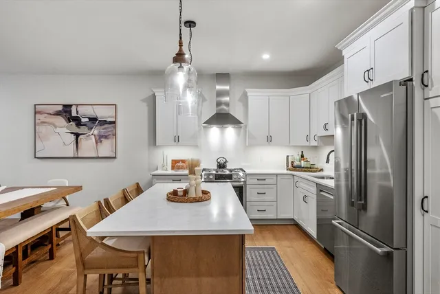 a kitchen with stainless steel appliances granite countertop a refrigerator a stove a sink dishwasher a dining table and chairs with wooden floor