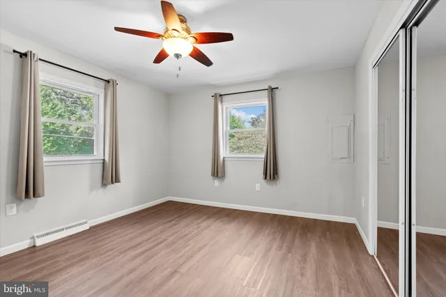 an empty room with wooden floor ceiling fan and windows