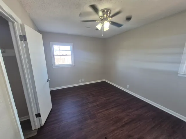 an empty room with wooden floor fan and windows