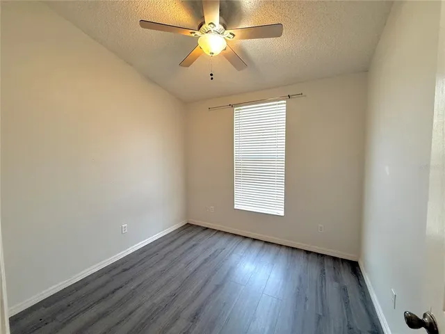 an empty room with wooden floor ceiling fan and windows