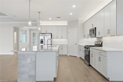 a kitchen with stainless steel appliances kitchen island granite countertop a stove a sink a refrigerator and white cabinets with wooden floor