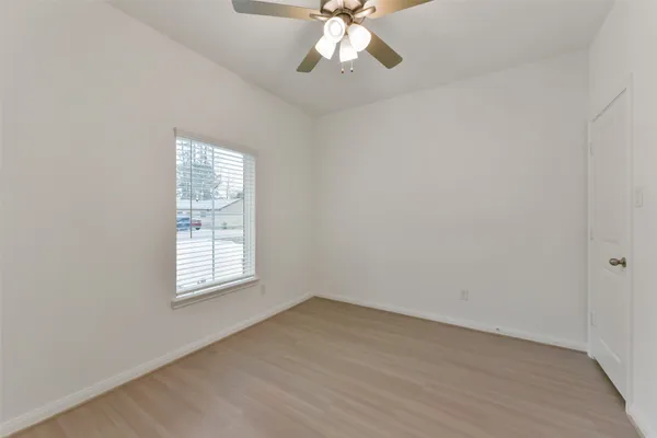 an empty room with wooden floor windows and fan