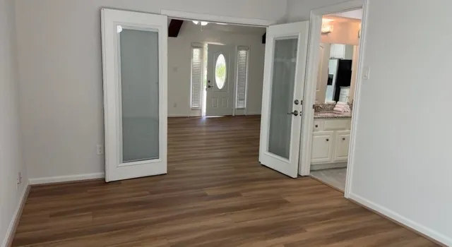 an empty room with wooden floor chandelier fan and windows