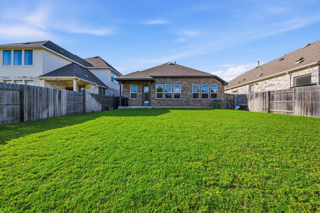 2032 Base Burner Path Leander, TX 78641 - Photo 33 of 34 Expansive backyard featuring a lush green lawn, full privacy fencing, and a brick-finish exterior with multiple windows