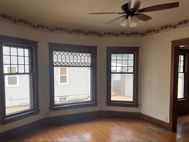 an empty room with wooden floor fan and windows