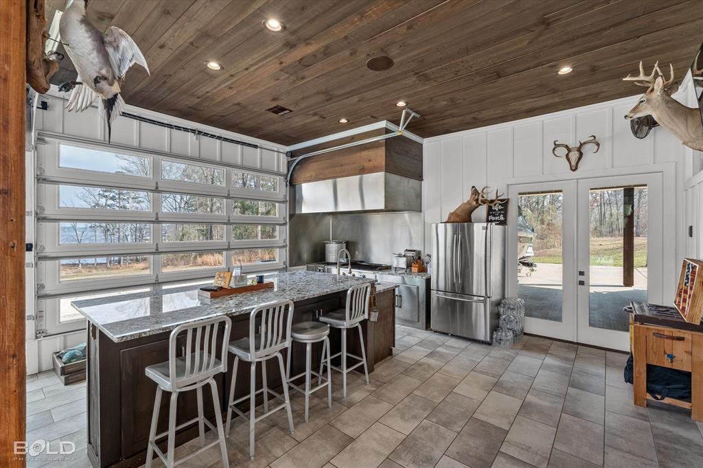 5296 Linton Cutoff Road Benton, LA 71006 - Photo 11 of 40 Two tone kitchen featuring a breakfast bar, french doors, freestanding refrigerator, a kitchen island with sink, and wood ceiling