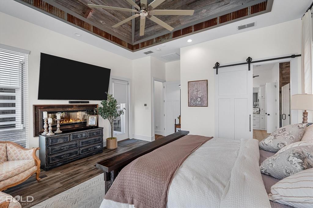 5296 Linton Cutoff Road Benton, LA 71006 - Photo 26 of 40 Bedroom with a barn door, wood finished floors, a multi sided fireplace, ensuite bathroom, and a ceiling fan