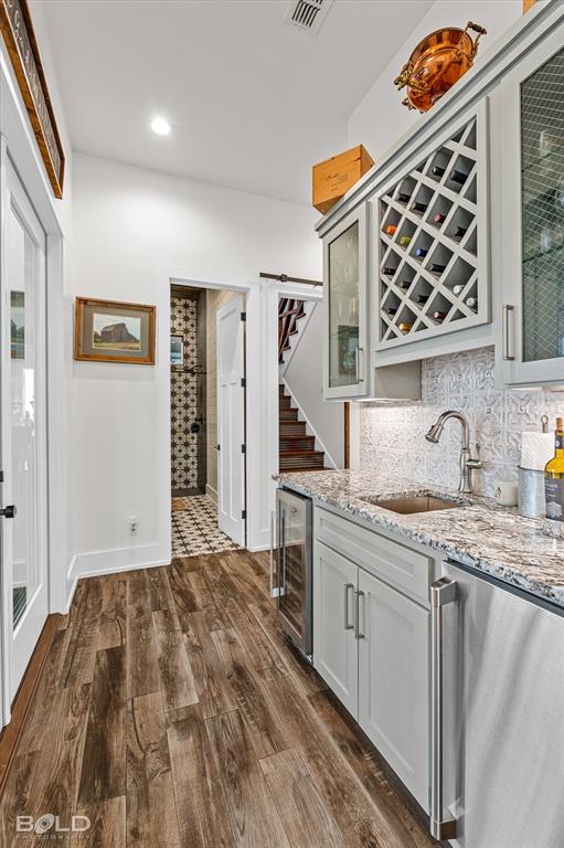 5296 Linton Cutoff Road Benton, LA 71006 - Photo 31 of 40 Indoor wet bar with light stone countertops, dark wood-style flooring, glass insert cabinets, beverage cooler, and decorative backsplash