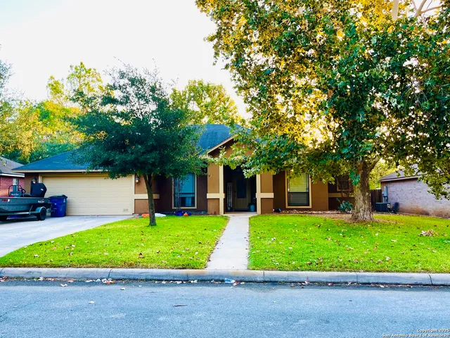 a view of a white house in front of a big yard with potted plants and large trees