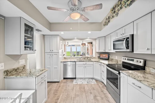 a kitchen with stainless steel appliances granite countertop a stove top oven a refrigerator a sink dishwasher and white cabinets with wooden floor