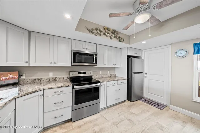 a kitchen with stainless steel appliances granite countertop a refrigerator a sink dishwasher a stove and white cabinets with wooden floor