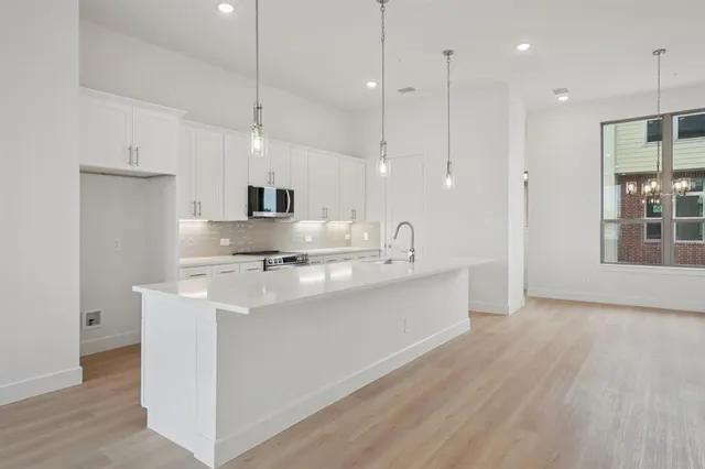 a kitchen with stainless steel appliances granite countertop a sink a microwave oven a refrigerator and white cabinets with wooden floor