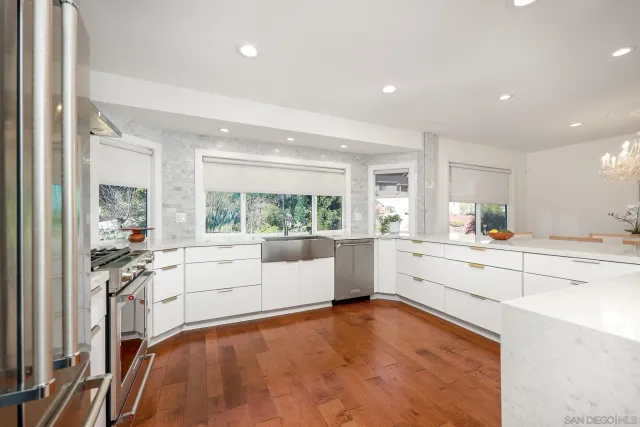 a large white kitchen with wooden floors and white stainless steel appliances